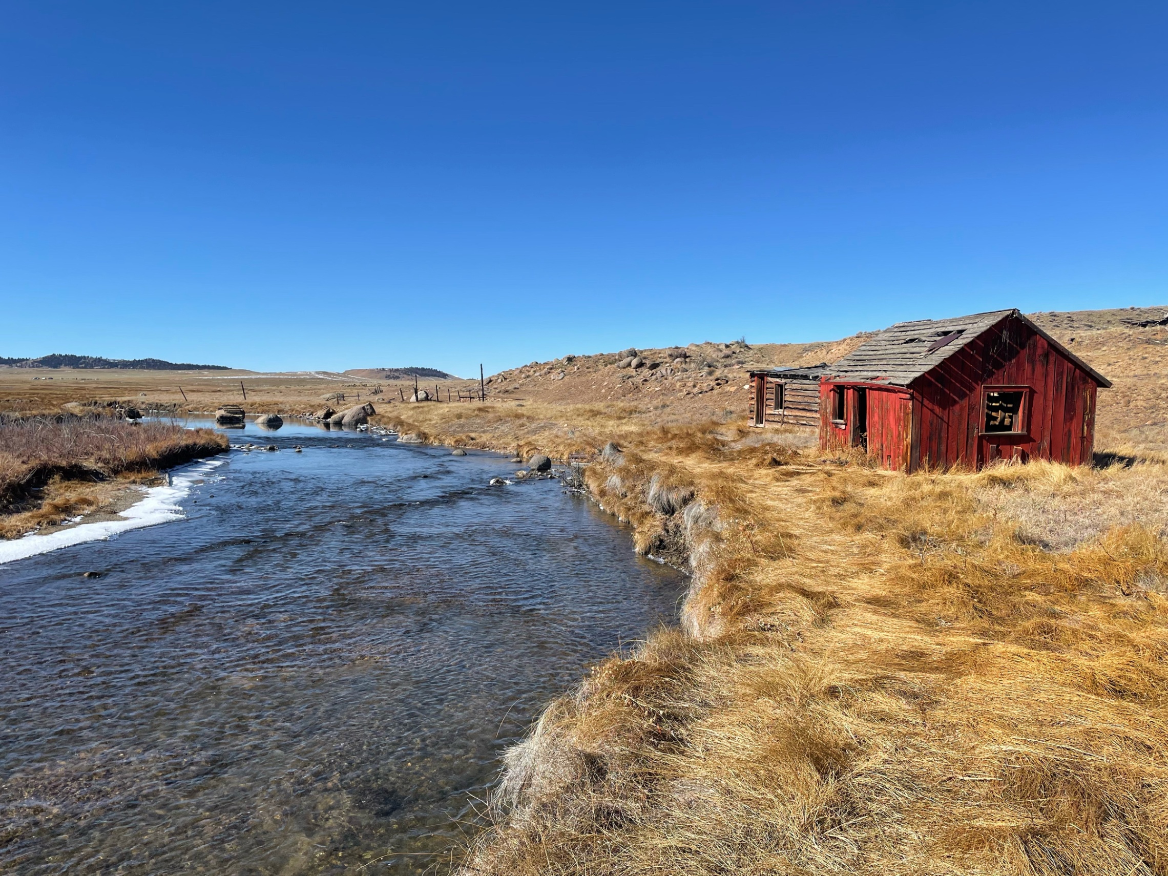 Red cabin beside flowing stream in high desert landscape — z is on the river